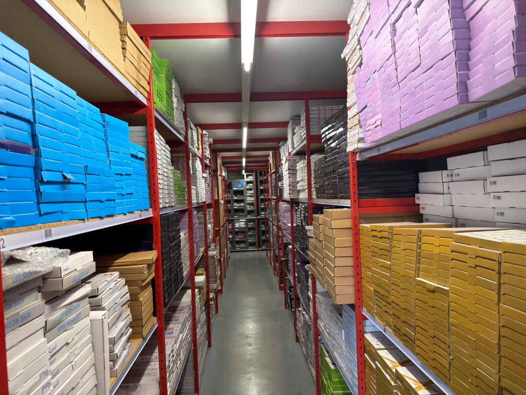 Warehouse aisle with colour-coded boxes on racks, each product in its own pick location.